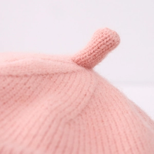 Macro shot of pink knit baby beret showing textured ribbed detail and top loop decoration