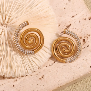Macro shot of 18K gold plated spiral earrings with white zircons on coral background