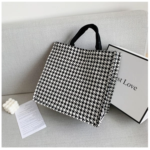 Detail view of stylish houndstooth tote bag on grey sofa with elegant gift box