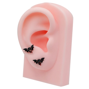 Gothic black bat stud earrings with red accents displayed on a pink ear model