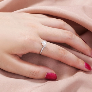 Elegant silver ring with white pearl and diamonds worn on finger over pink silk