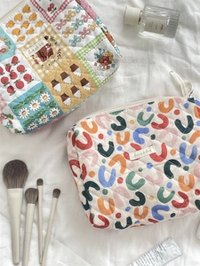 Flat lay of quilted floral cosmetic bags with perfume and makeup brushes on white sheet