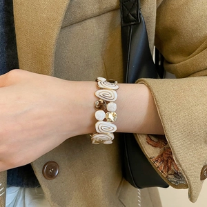 Close-up of a wide gold enamel stretch bracelet with spiral patterns on a female wrist