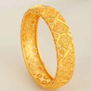 Macro detail of intricate gold hollowed floral filigree pattern on a vintage style bangle