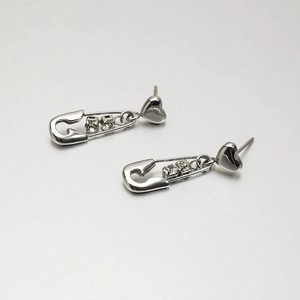 Close-up of silver steel safety pin earrings with heart studs and crystal accents