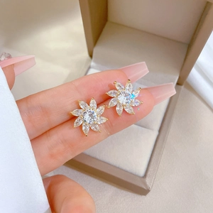 Macro detail of gold flower stud earring with micro-paved white zircon in a jewelry box