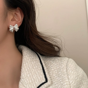 Close-up of polished silver bow stud earrings worn by a model in elegant white tweed