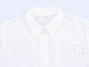Detail of white blouse featuring floral embroidery, lapel collar, and pin-tuck pleats