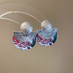 Détail de boucles d'oreilles rondes en bois avec paysage peint et finition métal brossé