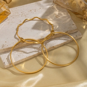 Three-piece set of golden geometric wave bangles on beige stone and silk backdrop