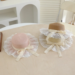 Detail of kids straw sun hats with wide lace trim and bows in pink, beige, and coffee