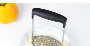 Détail macro du manche ergonomique noir et de la plaque perforée du presse-purée métal