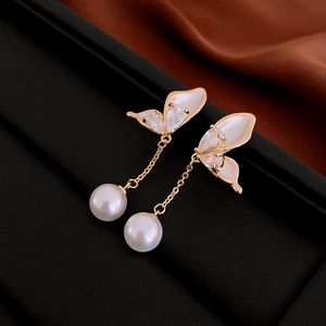 Macro shot of gold butterfly earrings with sparkling zircon and white pearl drop