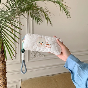 Detail of white quilted pouch featuring cute bear embroidery and colorful braided handle