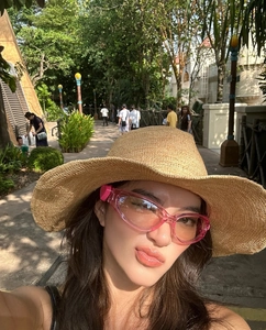 Pink heart-shaped Y2K sunglasses and straw sun hat worn in a casual outdoor setting