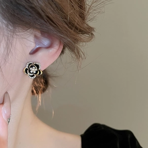 Détail de boucles d'oreilles camélia avec émail noir, bordure dorée et perle sur l'oreille