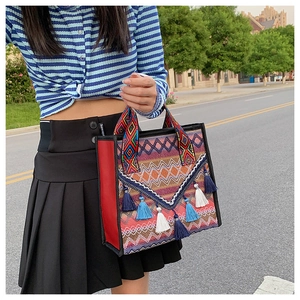 Détail d'un sac cabas bohème tissé avec des pompons colorés et des anses à motif ethnique