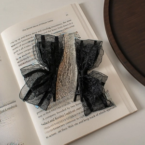 Detail of pair of black lace bow hair clips placed on a vintage English book page