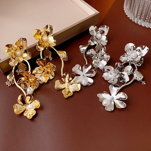 Detail of flower shaped earrings in gold and silver finish with pearl drop accents
