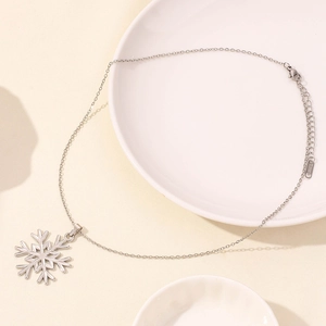 Macro detail of silver snowflake necklace in stainless steel on white ceramic plate