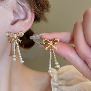 Detail of long bowknot earrings with pearls and zircons shown on a model for scale