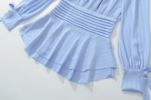 Détail d'un haut plissé bleu clair avec volants à la taille et poignets à nœuds lacés