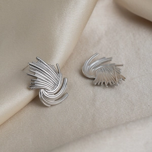 Detail view of silver stud earrings with radial firework texture on champagne satin