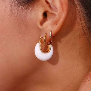 Close-up of a white C-shaped hoop earring and a small gold diamond-studded ring on ear