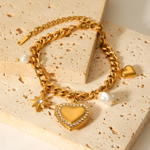Goldenes Gliederkettenarmband mit Stern-, Perlen- und Herzanhängern auf Stein-Hintergrund