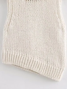 Detailed close-up of white chunky knit sweater featuring a unique asymmetrical hemline design