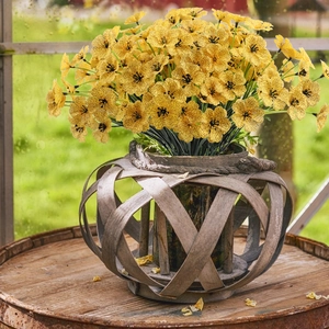 Yellow artificial violet bouquet in a woven glass vase with a soft garden backdrop