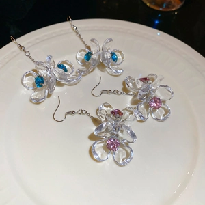Detailed shot of acrylic flower earrings with blue and pink rhinestones on a white plate