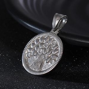 Macro shot of silver stainless steel tree of life pendant with textured edges on black background