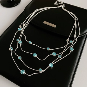Close-up of layered silver necklace with blue gemstones on black leather background