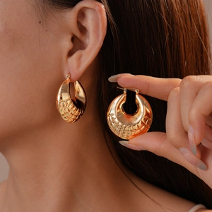 Detailed close-up of golden hollow hoop earrings with textured geometric grid pattern