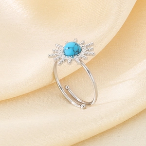 Detail of silver sunburst ring with round turquoise stone on cream silk fabric