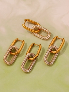 Détail de boucles d'oreilles dorées en maillons avec zircons blancs sur du marbre
