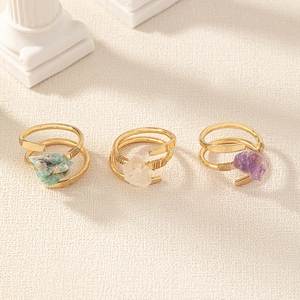 Three-piece set of golden rings with purple and green raw stones on roman columns