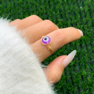 Detail of handmade gold wire-wrapped ring featuring a purple evil eye bead on finger