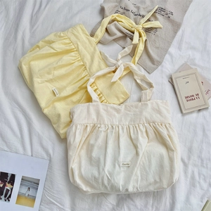 Detail of canvas tote bags with ruffled edges and knotted strap in beige and yellow