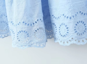 Gros plan sur un tissu en coton bleu clair avec broderie florale et détails ajourés