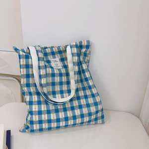 Detail of blue and green checkered canvas tote bag with floral patterns on a white chair