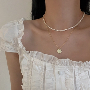 Detail of layered freshwater pearl and gold pendant necklace on white lace blouse