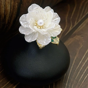 Elegant white camellia flower brooch with pearl accents and sparkling rhinestones on black stand