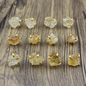 Twelve natural irregular raw stone stud earrings with golden claw settings on wood background