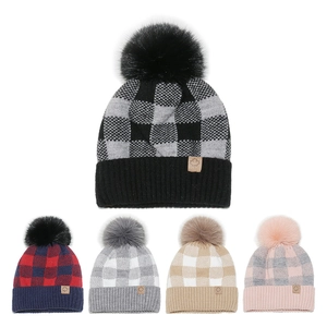 Detailed view of plaid knit beanies with faux fur pom-poms and leather maple leaf patch