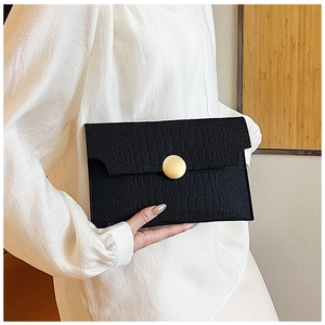 Detail of black crocodile texture envelope clutch bag with a round gold metal buckle
