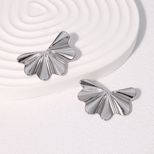 Close-up of silver butterfly fan earrings with pleated texture on white stone tray
