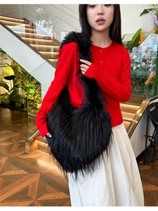 Close-up of black faux fur shoulder bag with tassel, styled with a red knit cardigan
