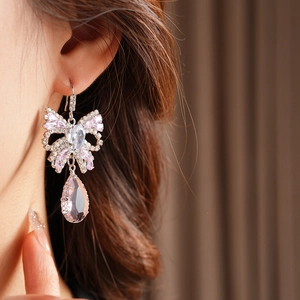 Detailed close-up of bow knot earrings with pink water drop crystal pendant on model